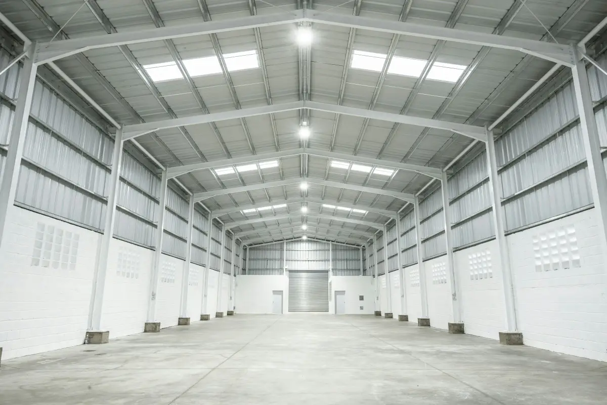 Empty refurbished industrial unit with white steel portal frame, rooflights, LED high-bay lights and a roller shutter door