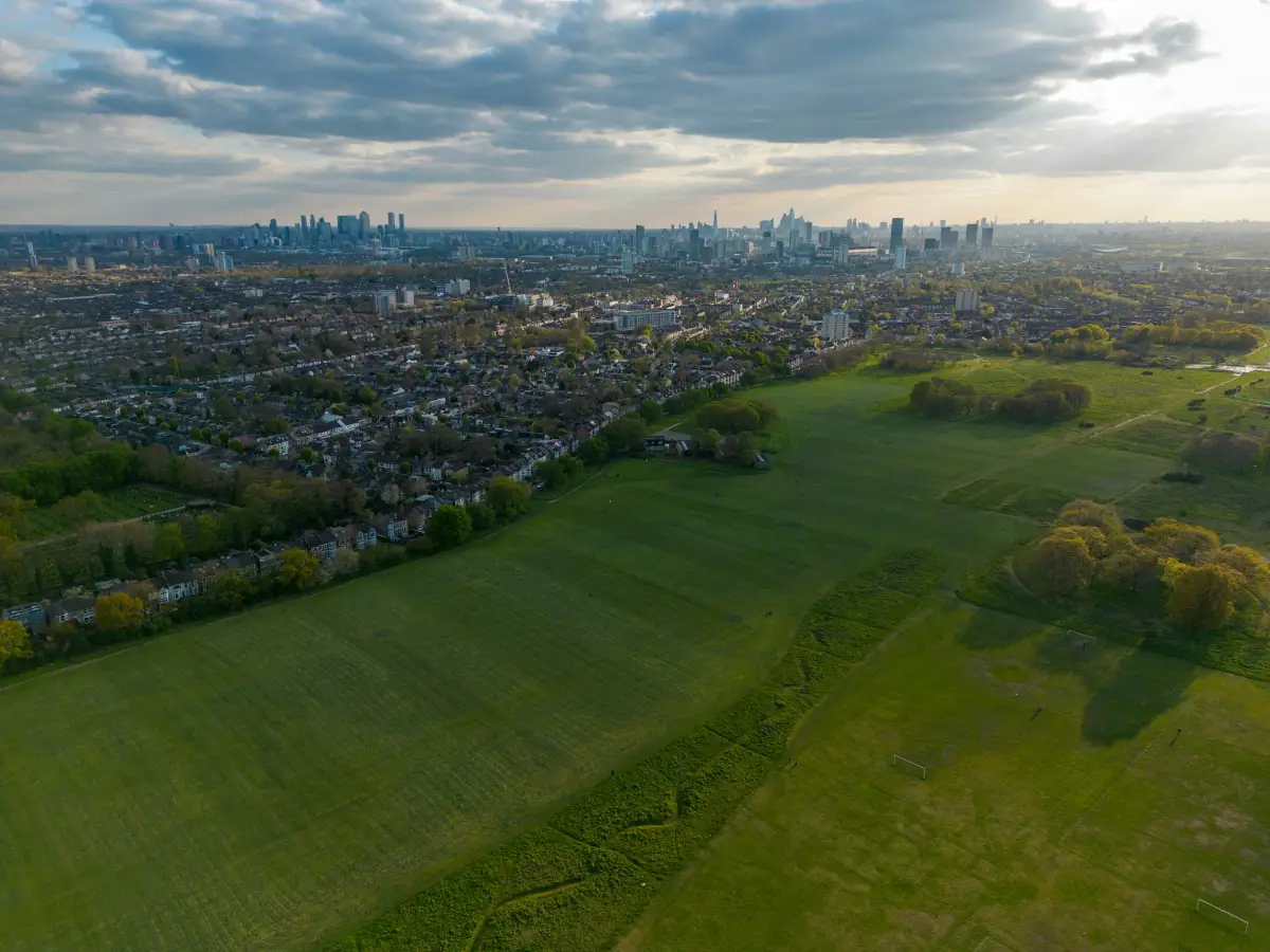 Aerial view over green playing fields and terraced streets in east London with the City and Canary Wharf skyline behind