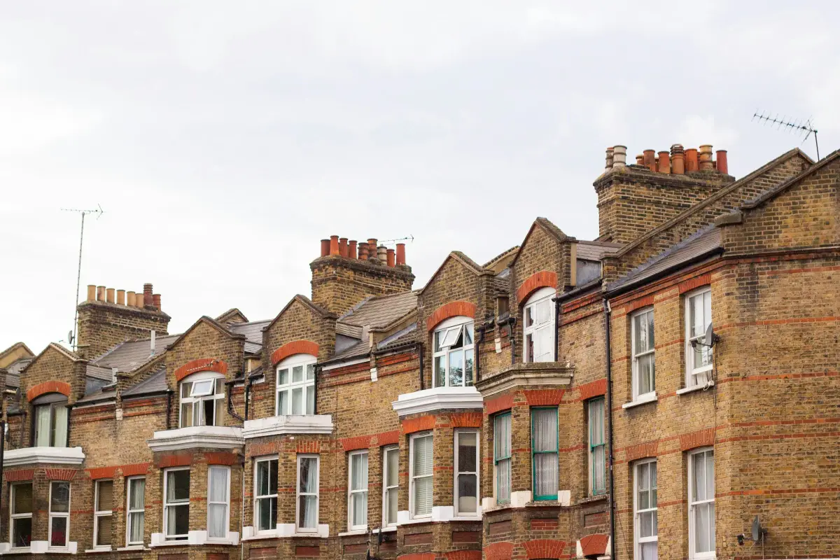 Row of Victorian yellow-brick terraced houses with red brick arches, bay windows and clay chimney pots under a pale sky