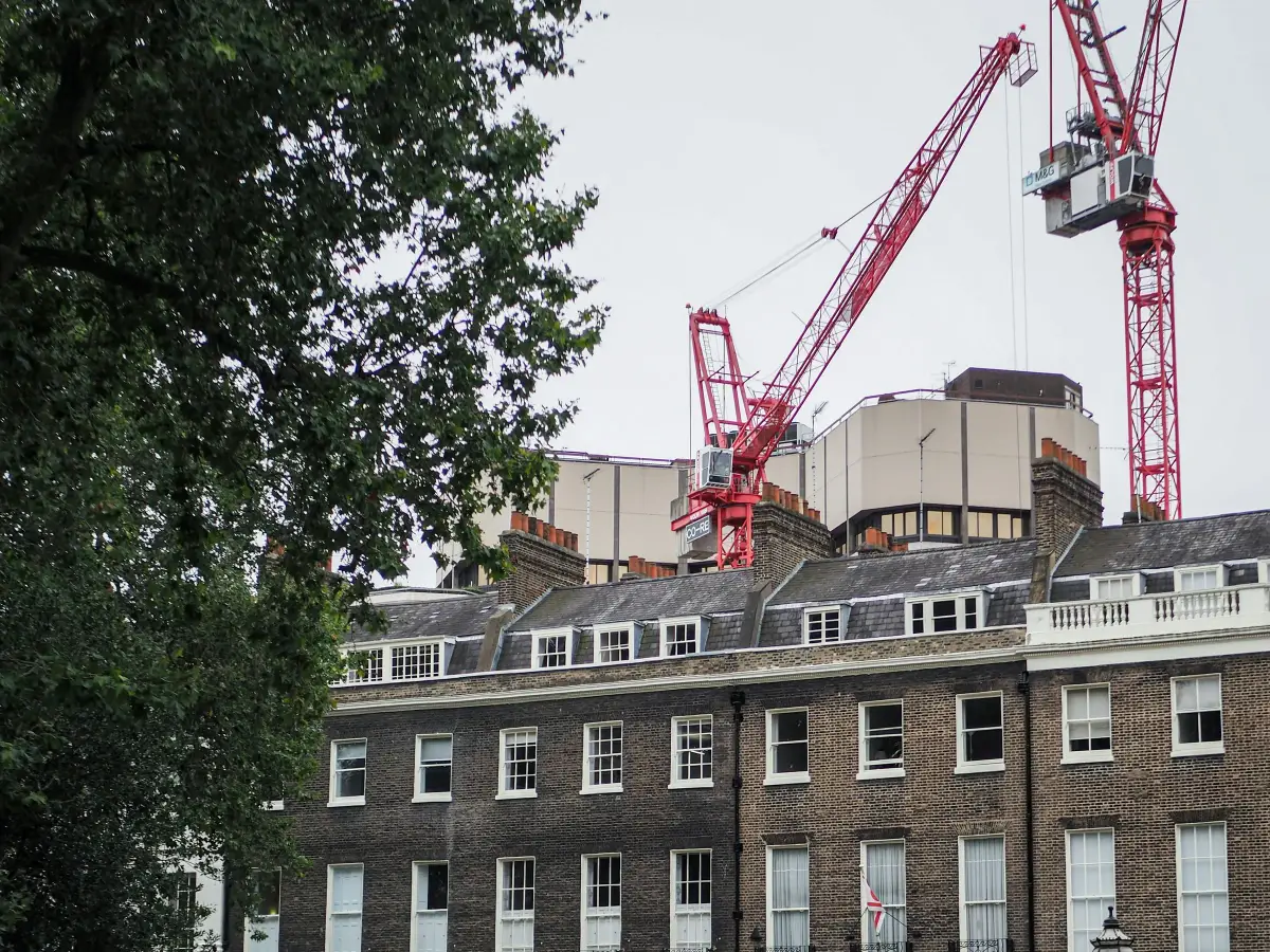 Red tower cranes rising behind a Georgian brick terrace on a London square
