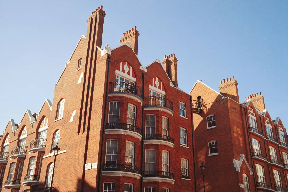 Red-brick London mansion block with white sash windows, balconies and tall chimneys against a clear sky