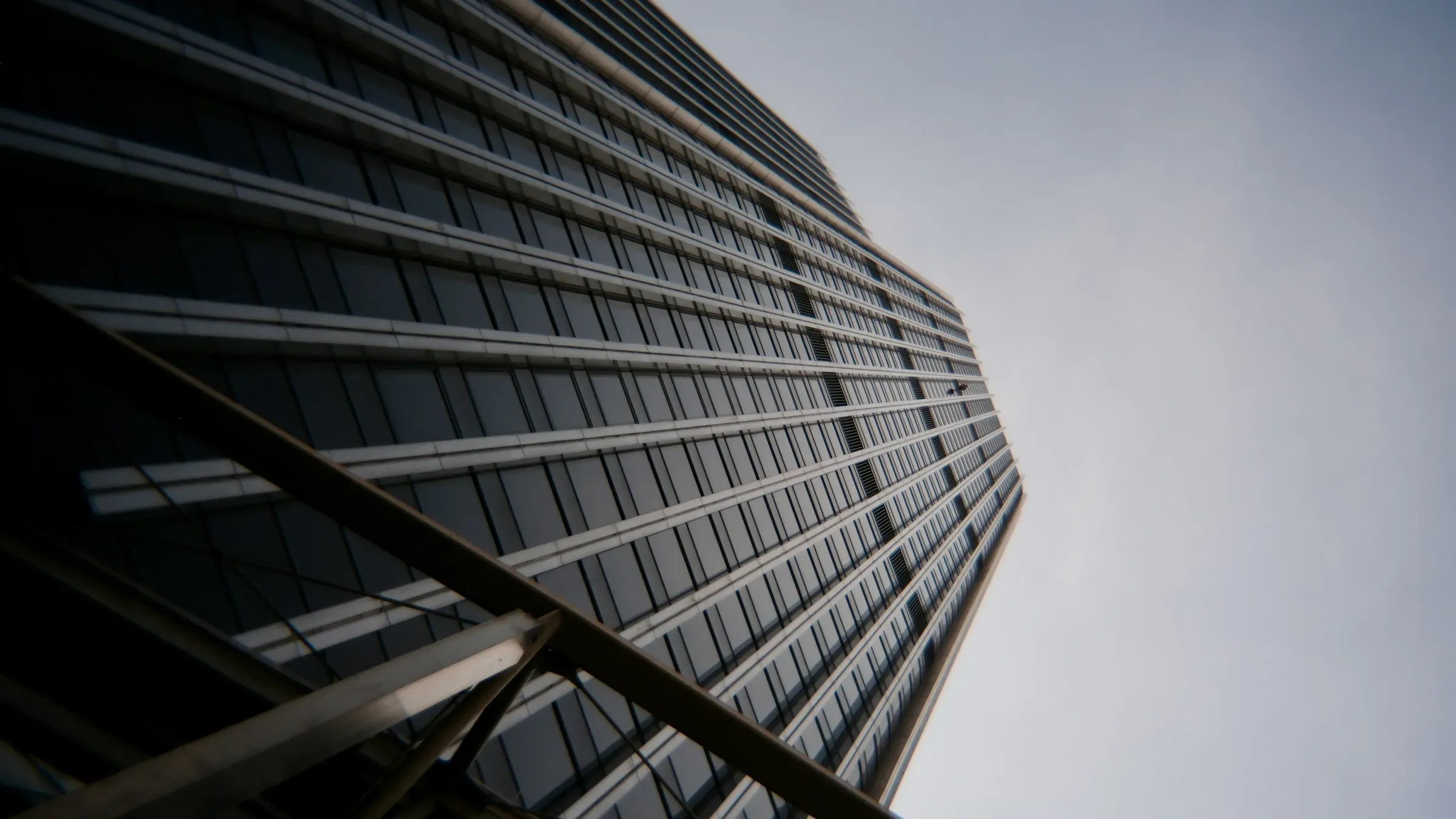 Glass-fronted London office tower seen from below against a pale sky
