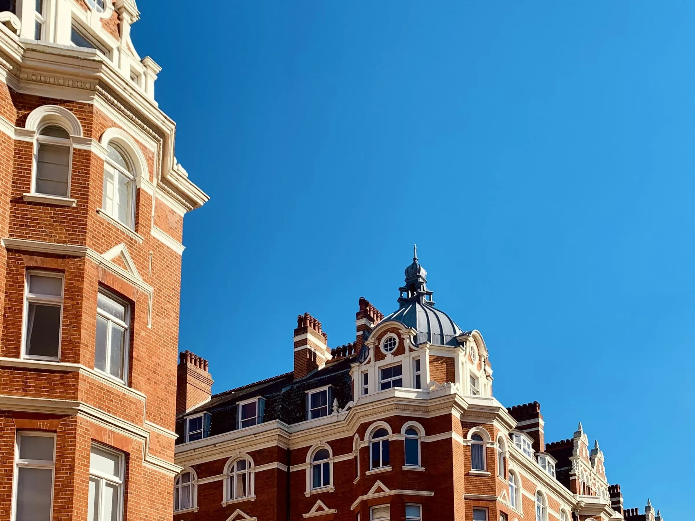Red-brick Edwardian mansion blocks with white stone dressings and a domed corner turret under a blue sky