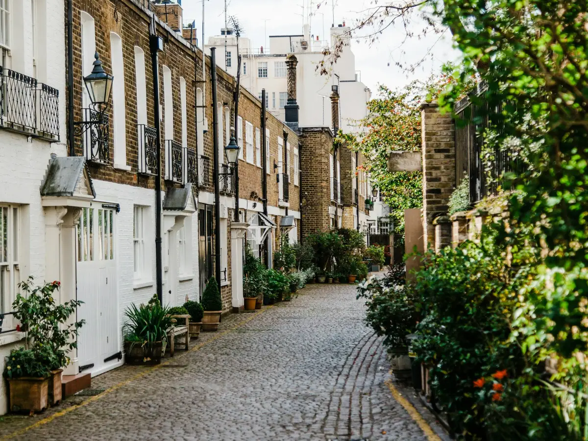 Cobbled mews street in Kensington lined with white and brick houses, lanterns and potted plants