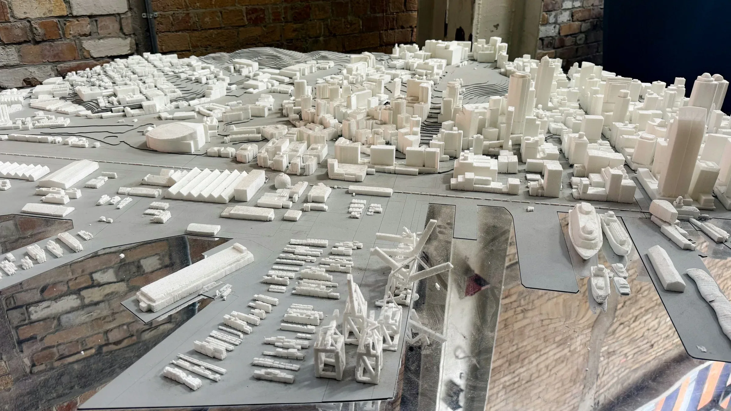 White architectural scale model of a city waterfront with high-rise blocks, quays and cranes on a studio table