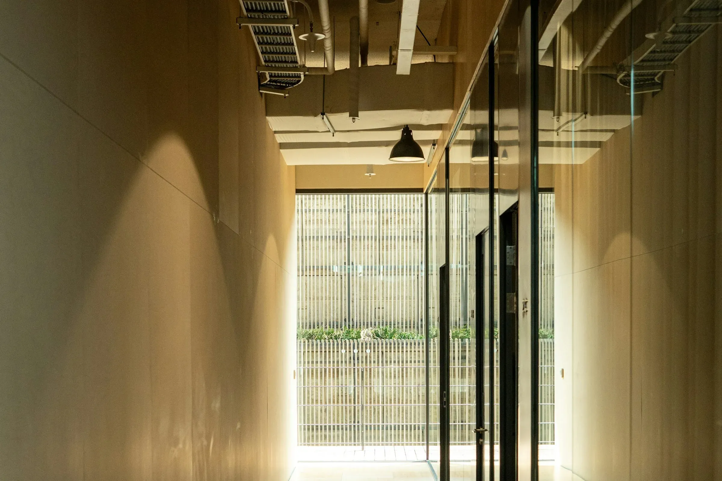 Office corridor with glass partitions, timber-faced walls, an exposed ceiling with cable tray and black pendant lamps