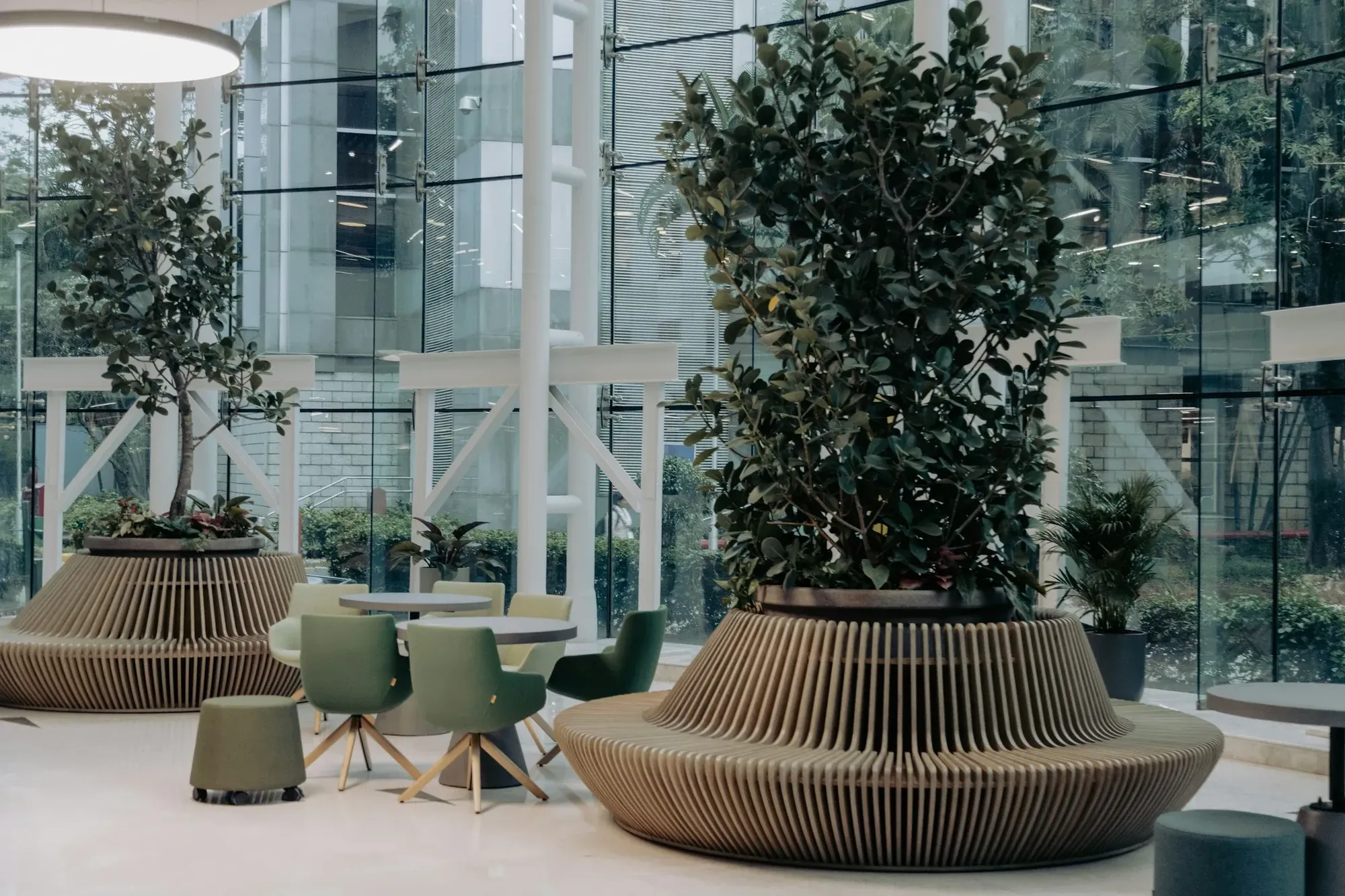 Office atrium with large planters, trees and green chairs beside a glass wall