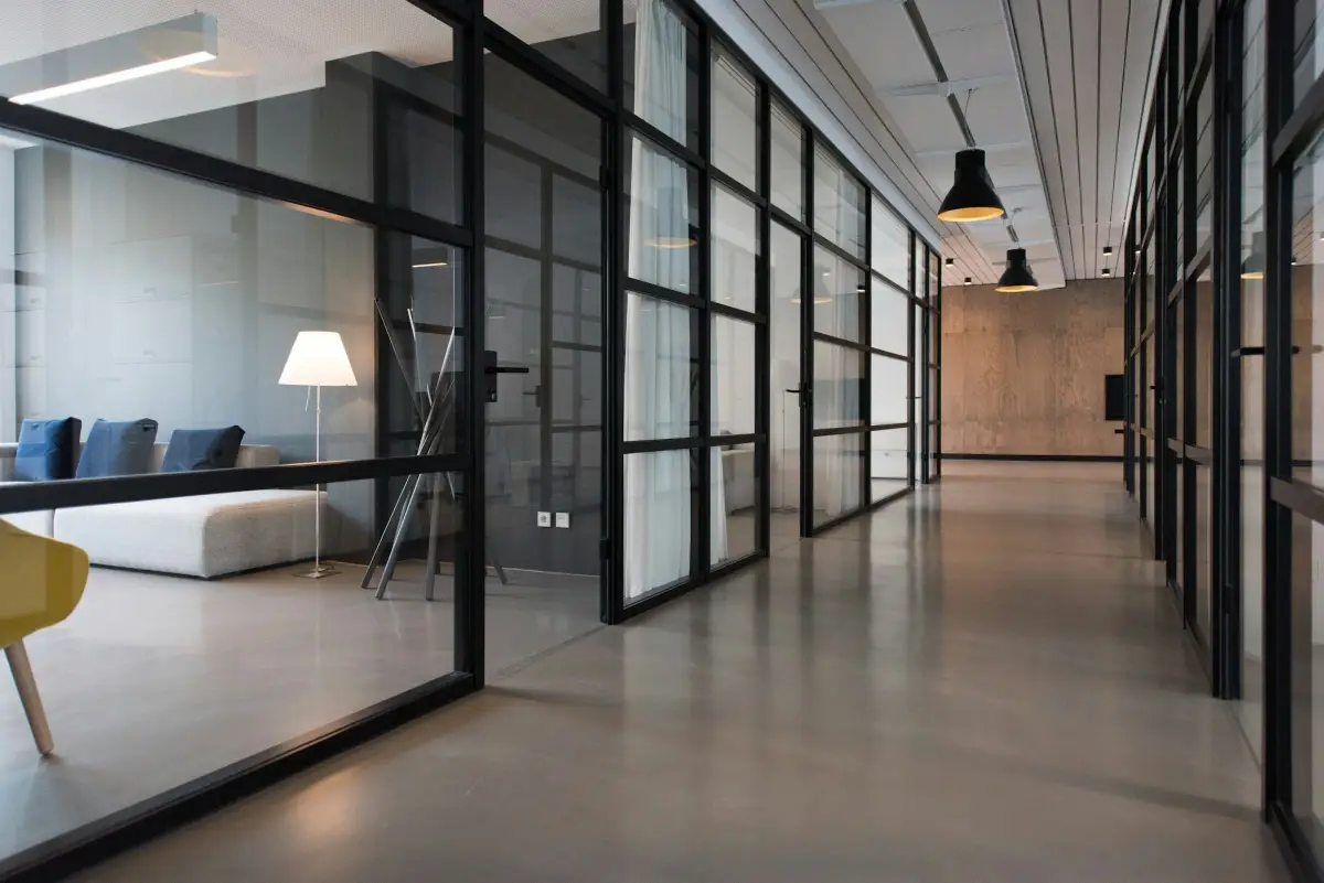 Office corridor with black-framed glass partitions, a polished floor and black pendant lights