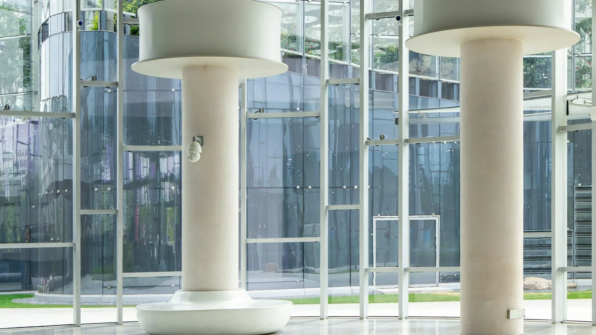Glazed office lobby with white drum-topped columns, a polished reflective floor and a curved glass wall