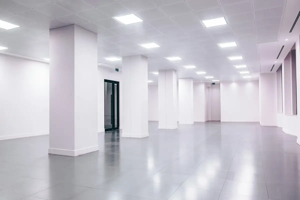 Empty open-plan office floor with a suspended ceiling grid, recessed LED panels, white columns and a polished tiled floor
