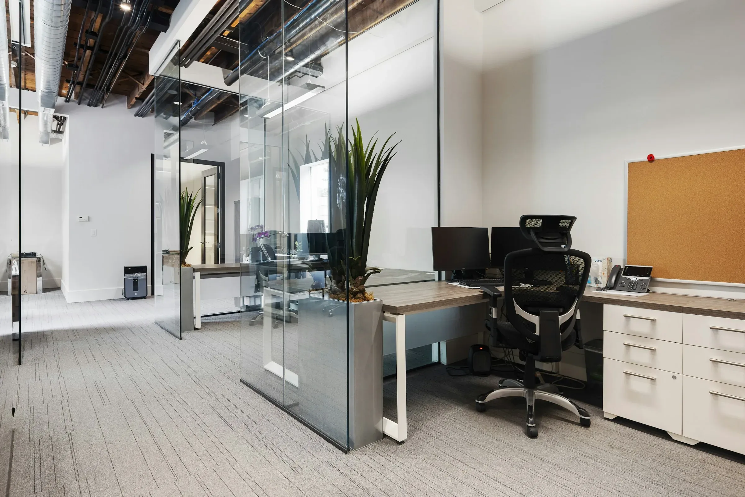 Office with full-height glass partitions, an exposed ceiling and a desk with a black mesh chair