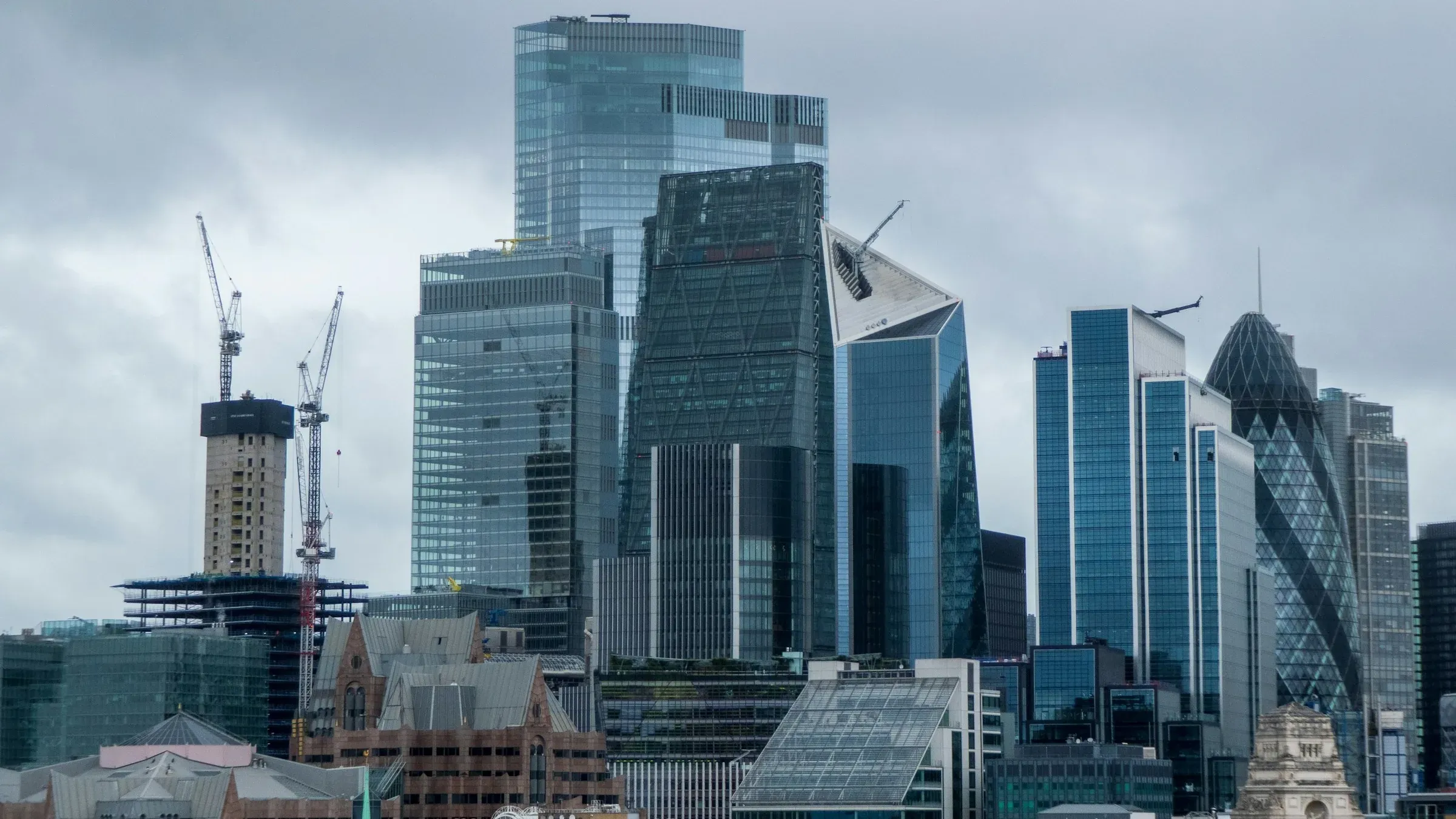 Tower cranes over an office tower under construction beside finished glass towers in the City of London