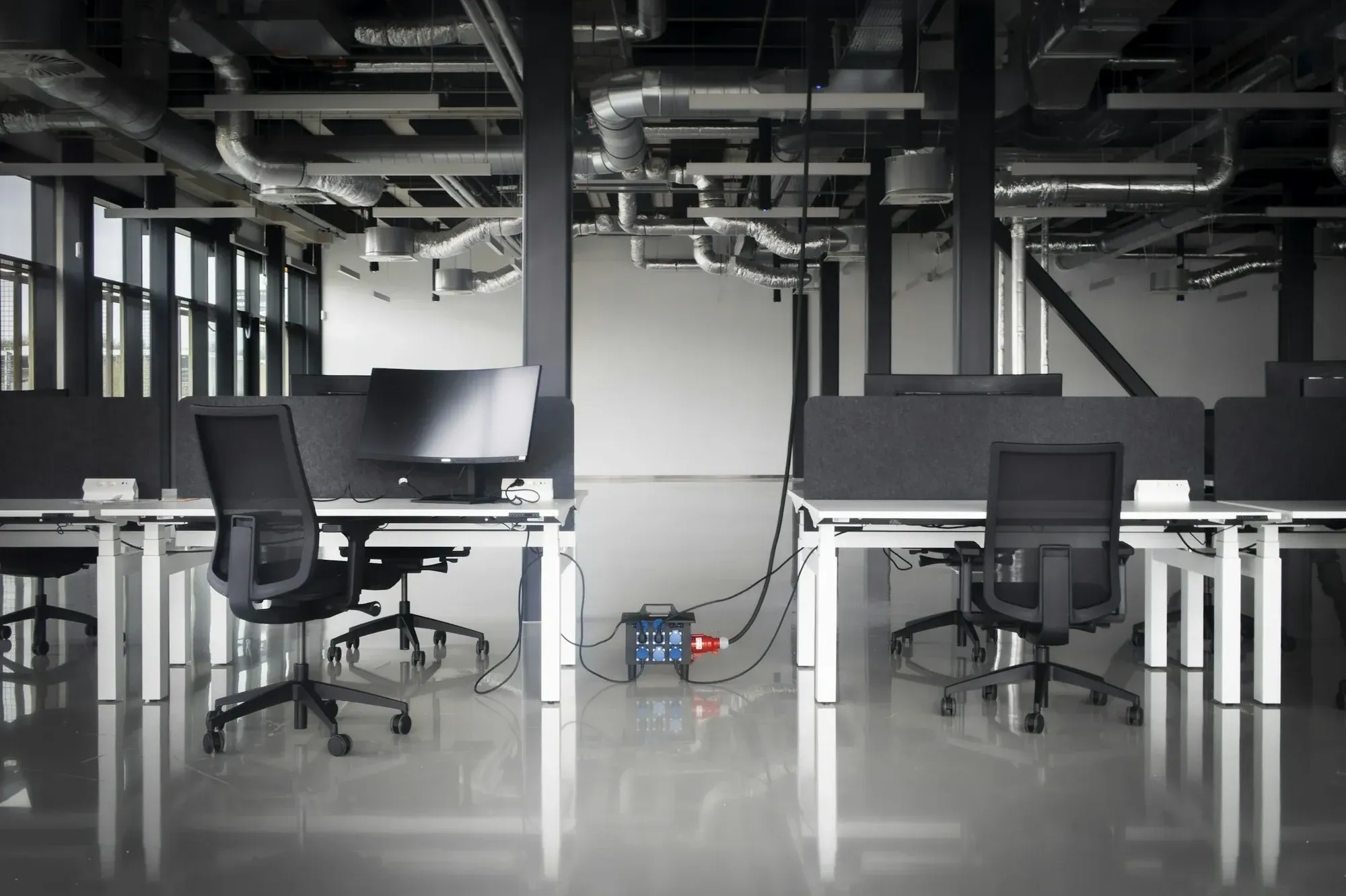 Office floor nearing completion, with exposed ductwork and services above new desks and a temporary power unit