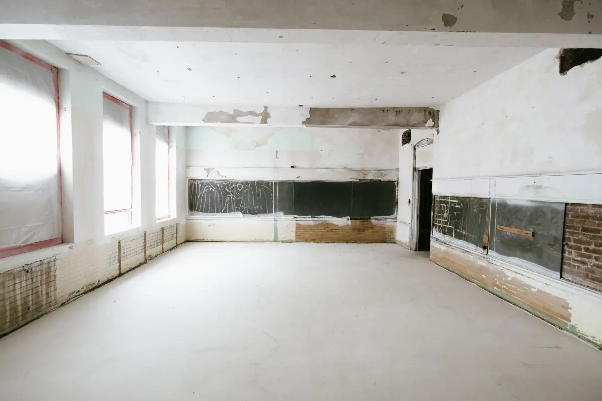 Empty room stripped back for refurbishment, with patched walls, bare floor screed and tall windows