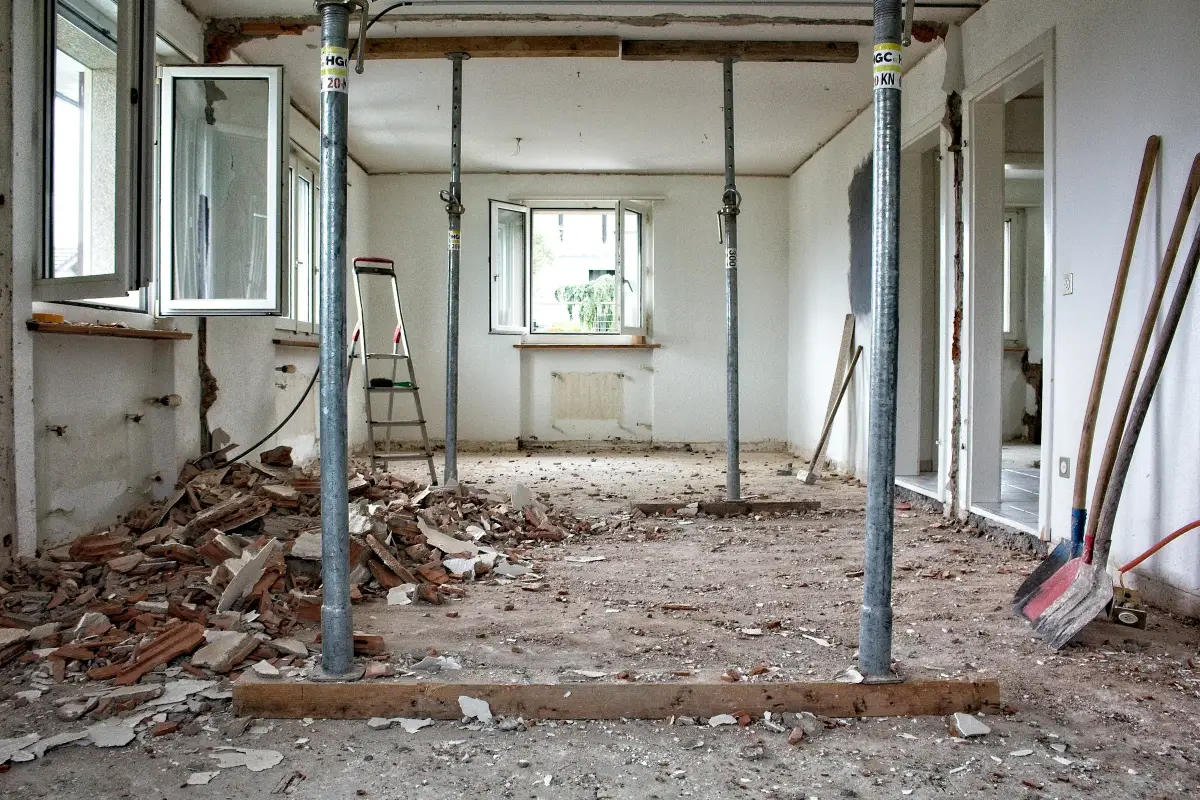 Room under renovation with steel props holding the ceiling, rubble on the floor and shovels against the wall
