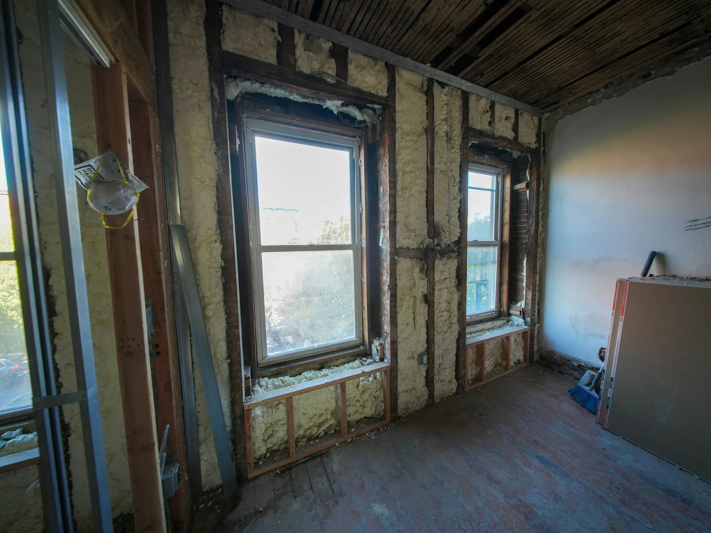 Stripped-back room mid-refurbishment with exposed insulation around the window frames and plasterboard stacked against the wall