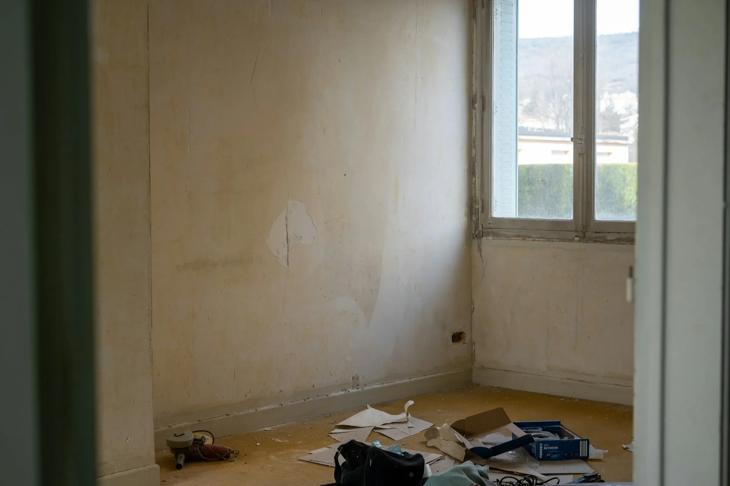Empty room mid-refurbishment with bare walls, a window and tools and packaging on the floor