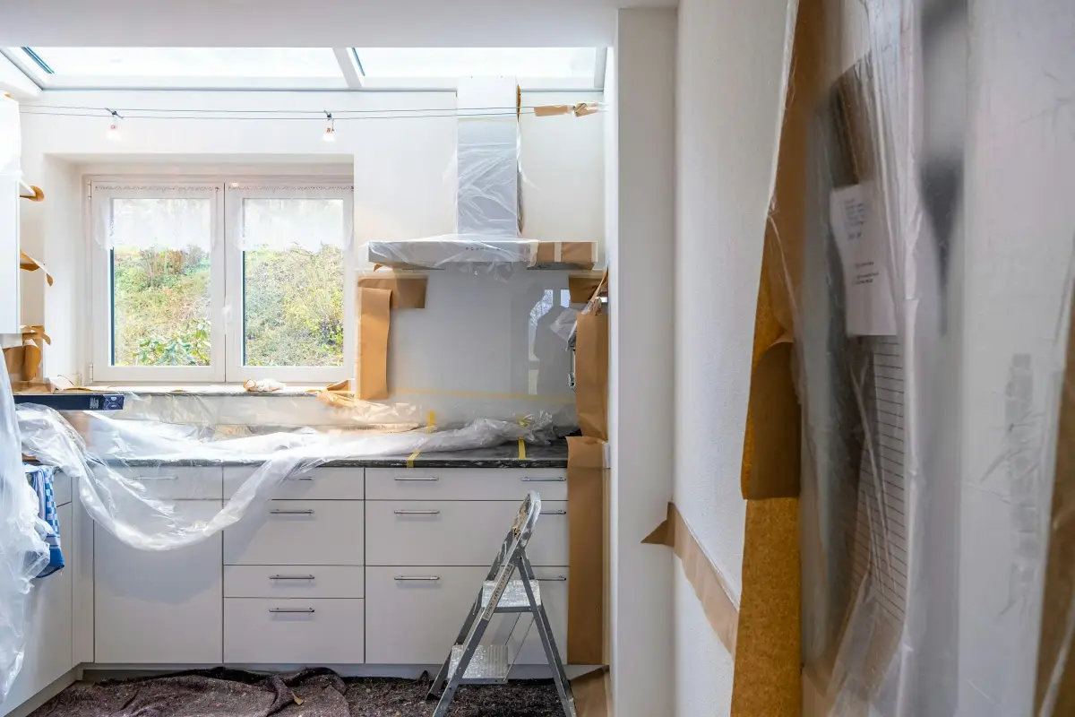 Kitchen mid-renovation with units and worktops wrapped in plastic sheeting and a stepladder on the floor