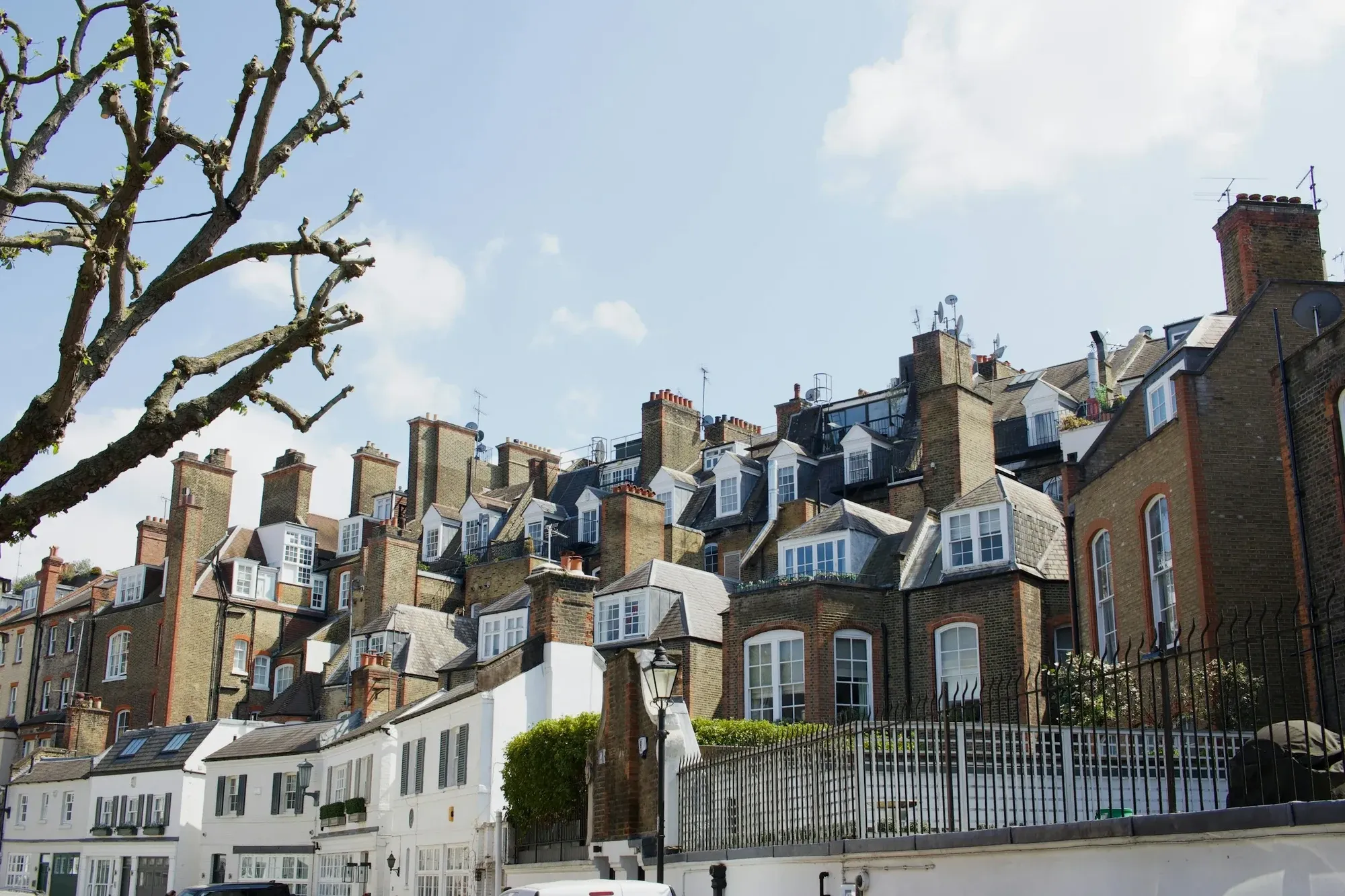 Row of London period houses with tall chimneys and dormer windows under a blue sky