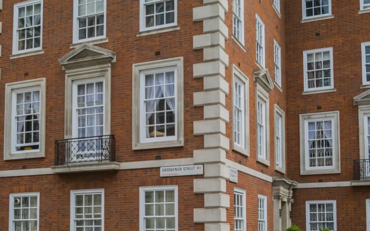 Red-brick London mansion block with white sash windows, stone quoins and a wrought-iron balcony