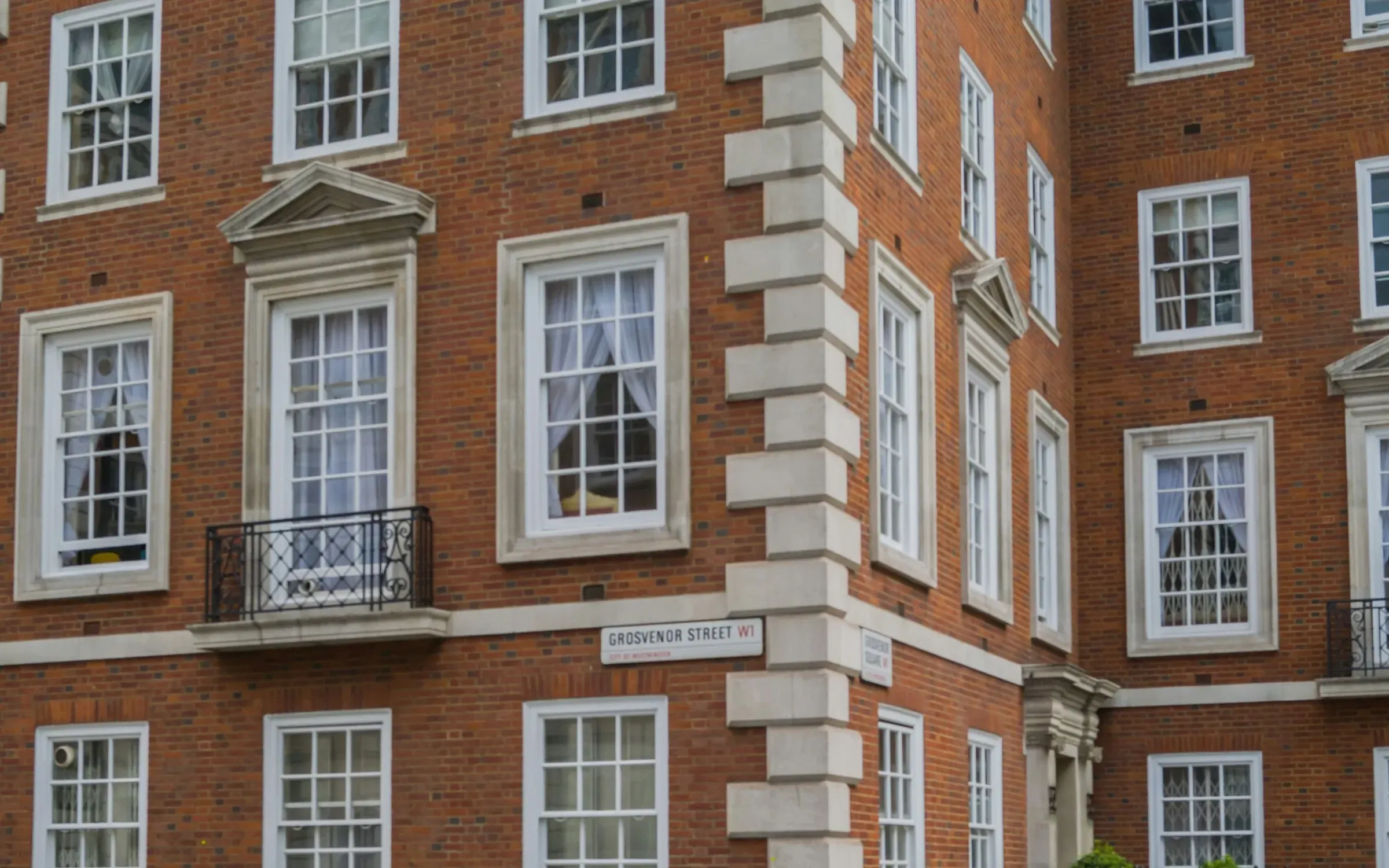 Red-brick London mansion block with white sash windows, stone quoins and a wrought-iron balcony