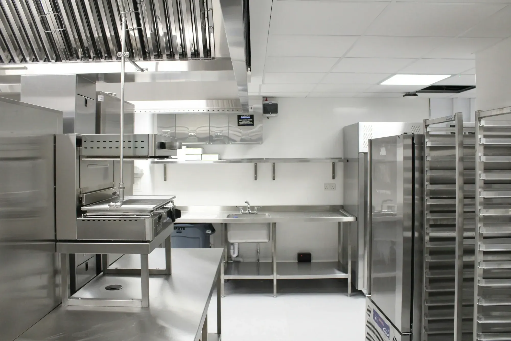 Back-of-house commercial kitchen with stainless steel worktops, refrigeration, racking and an extraction canopy