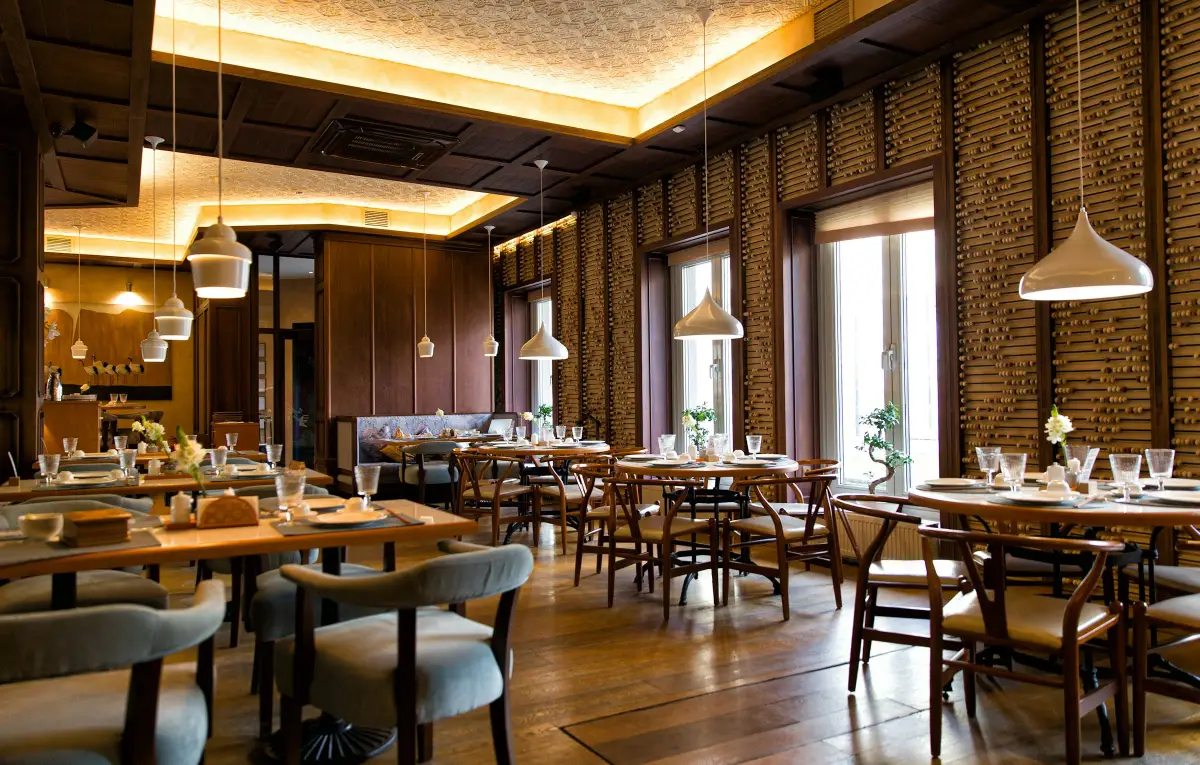 Restaurant dining room with timber panelling, pendant lights, a lit coffered ceiling and tables laid for service