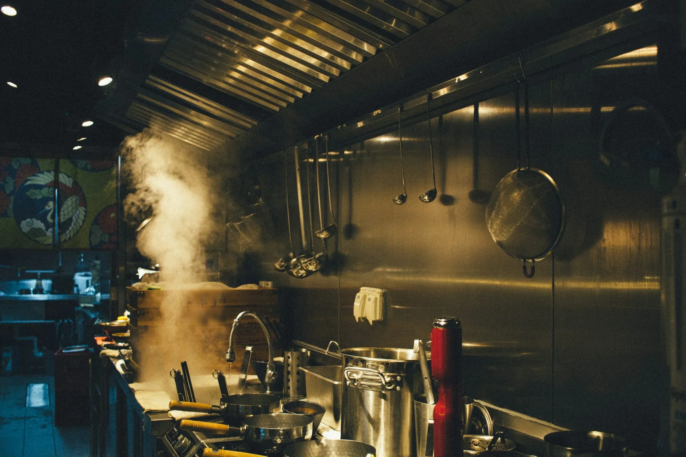 Steam rising from a stainless steel cooking line under a commercial kitchen extract canopy