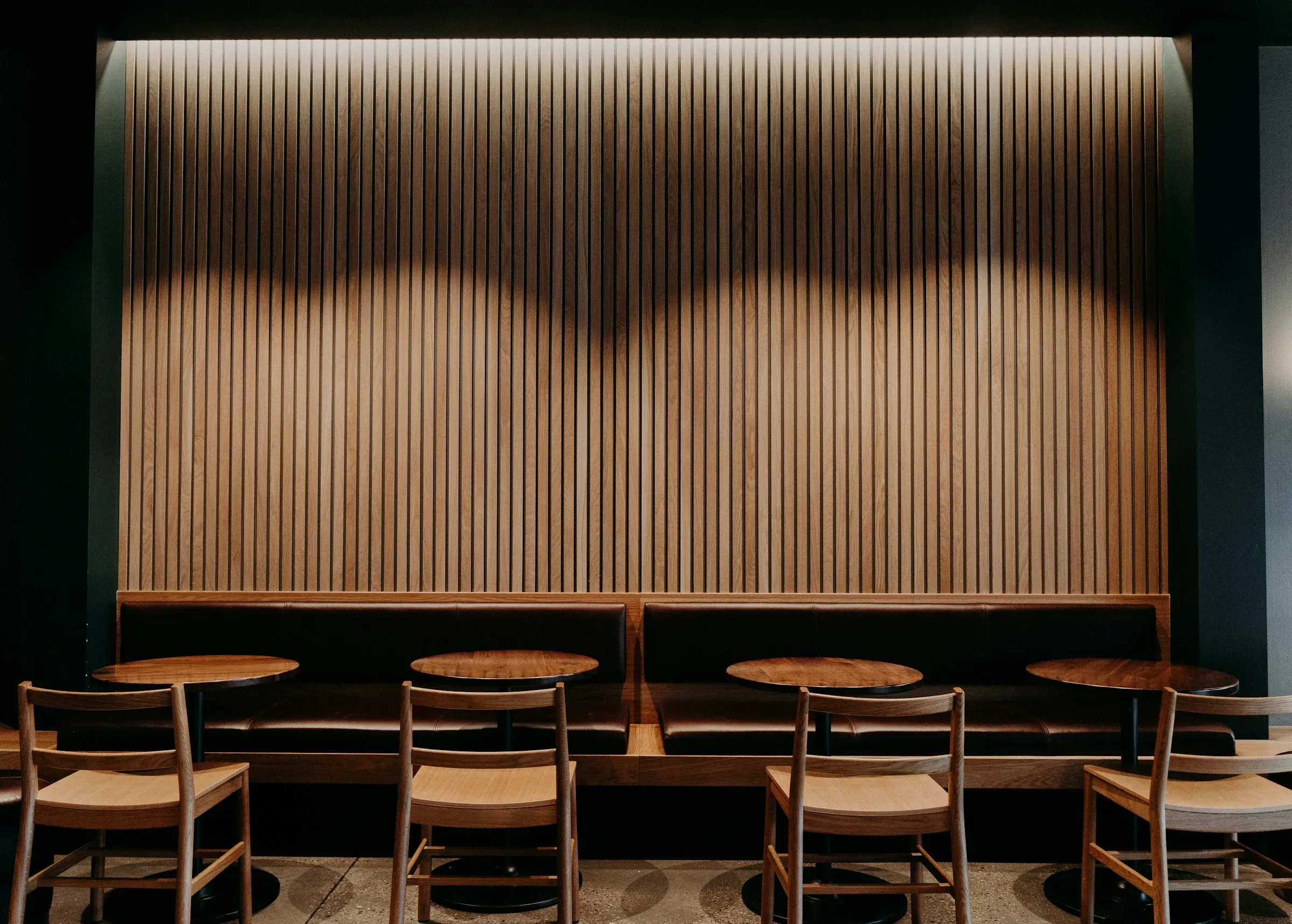 Oak slatted wall above leather banquettes with round bistro tables and timber chairs