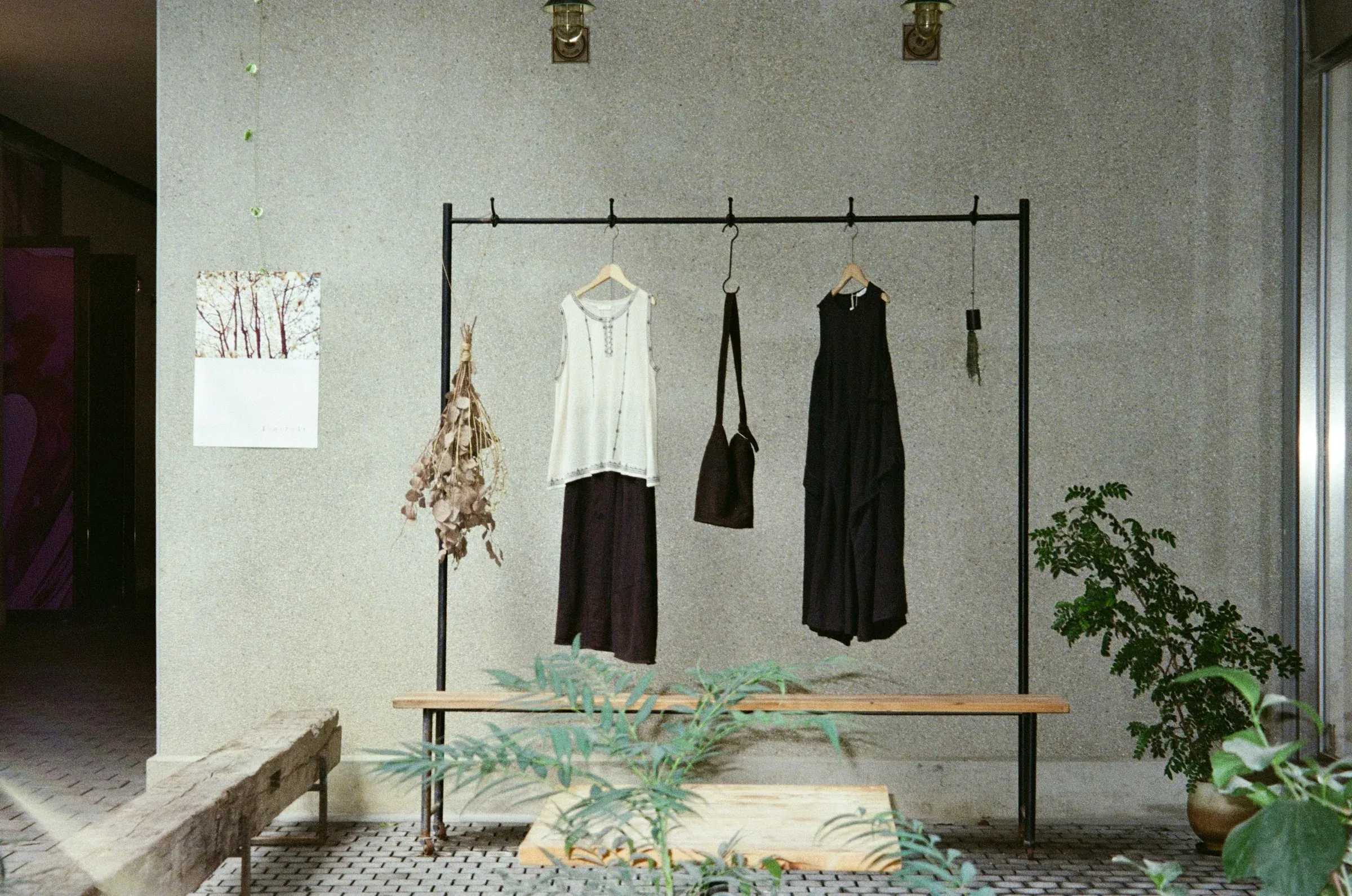 Freestanding black clothing rail and timber bench against a concrete wall, with plants