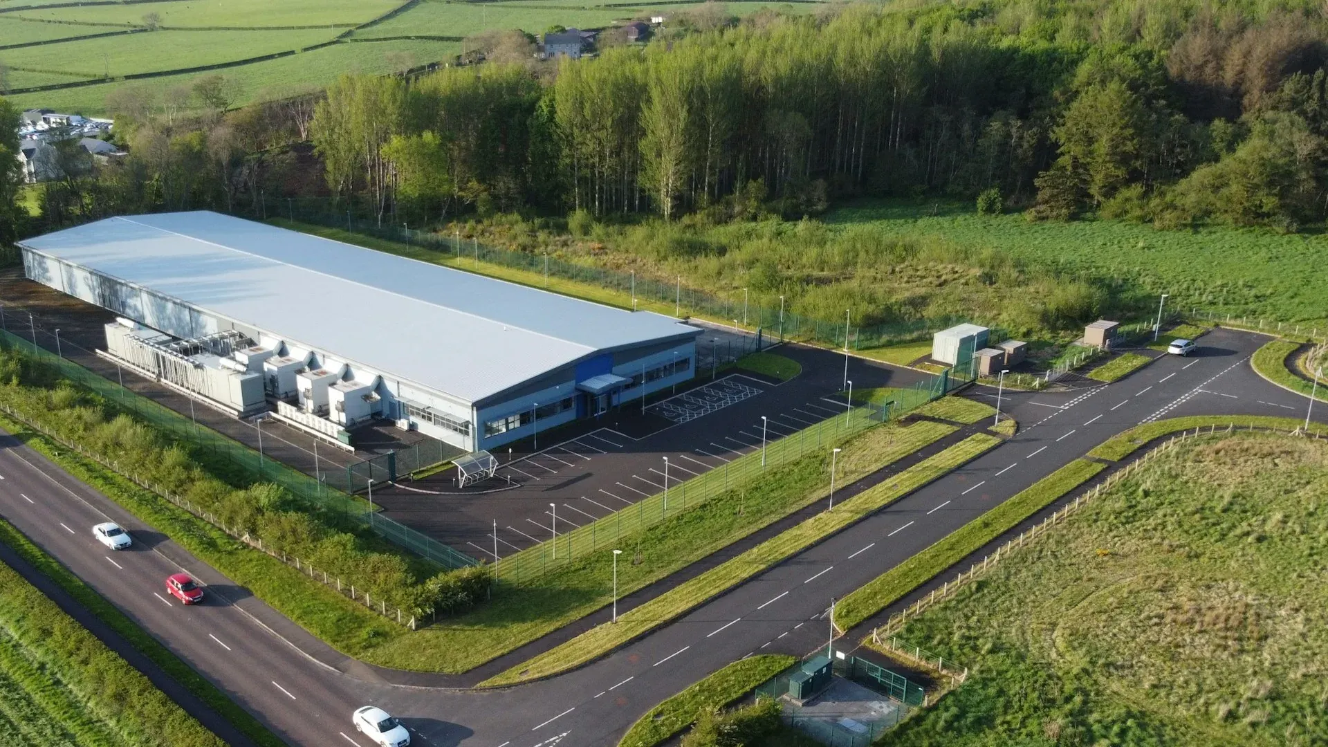 Long industrial shed with a pale profiled metal roof beside a road