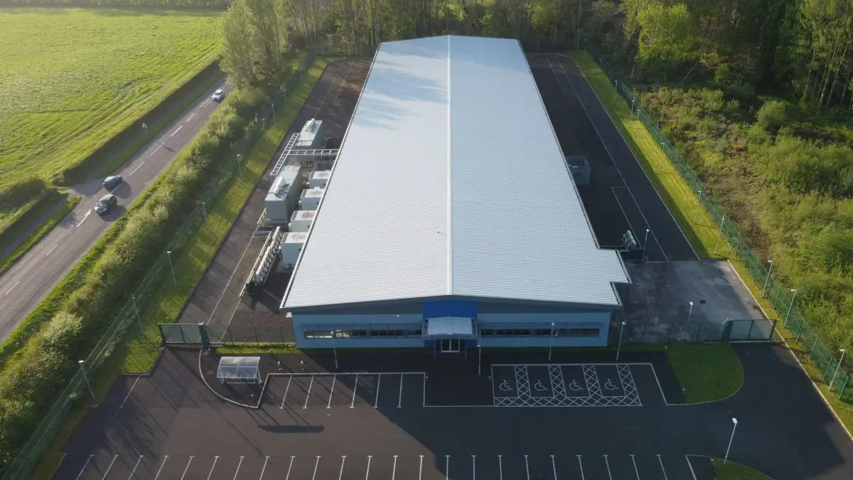 Aerial view of a large steel-framed industrial building with a long profiled metal roof and plant along one side