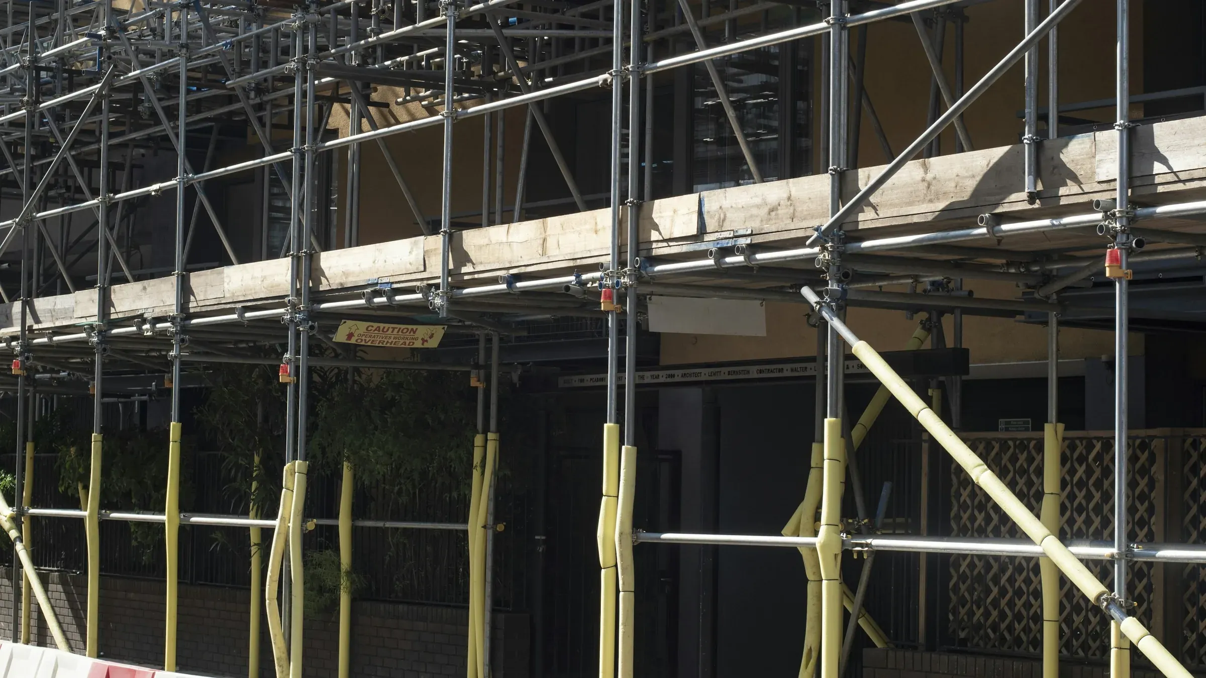 Scaffolding around a building facade with red and white road barriers along the pavement