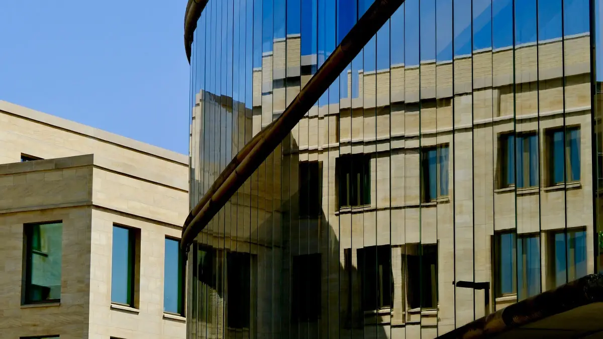 Modern glass education building reflecting a stone building beside it on a UK campus