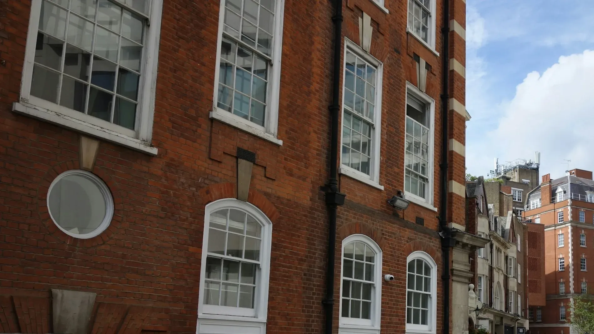 Red brick Victorian building with white sash windows beside a London street under a blue sky