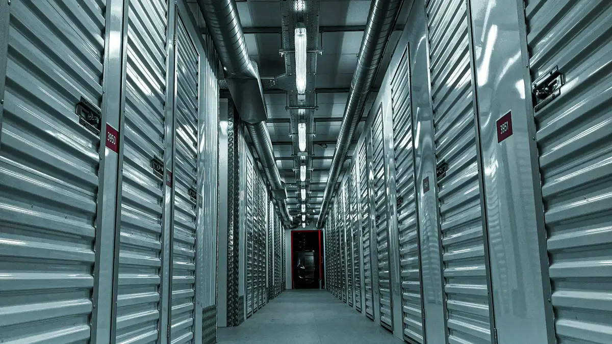 Long corridor of silver roller-shutter storage unit doors with ducting and lighting overhead