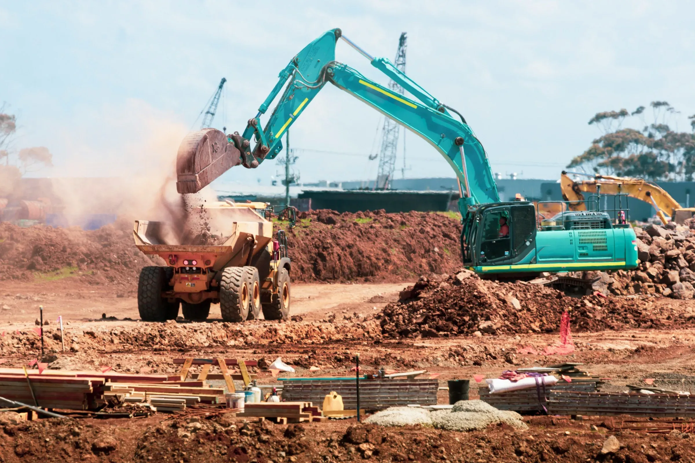 Excavator loading soil into a dumper during earthworks on an open site