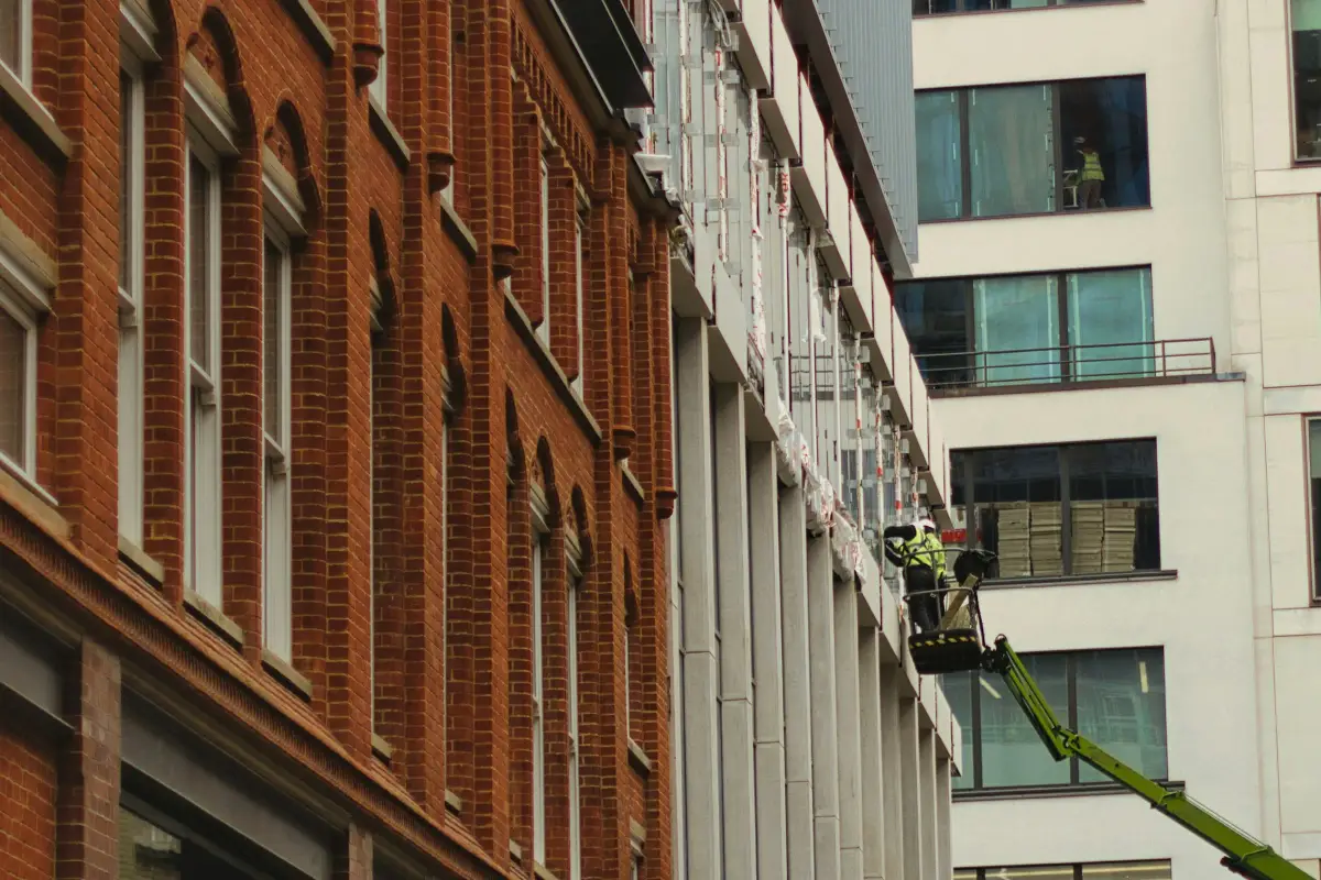 Workers on a mobile elevating platform fixing the facade of a new building next to a red-brick terrace in London