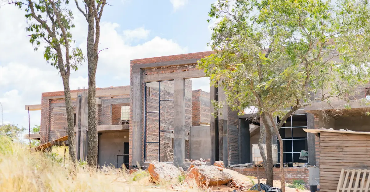 Unfinished brick and concrete building left abandoned among long grass and trees