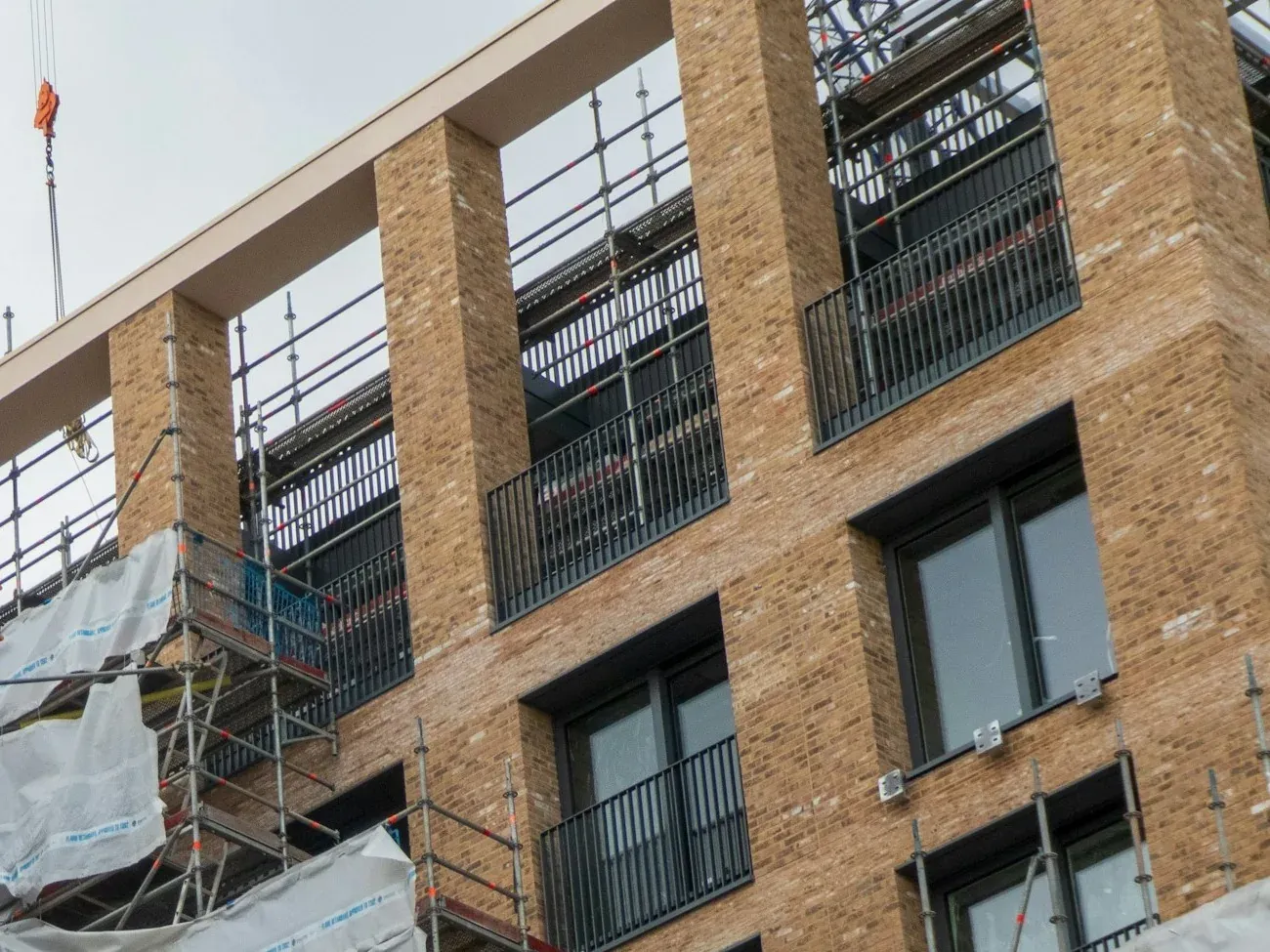 Brick-clad apartment block under construction in Farringdon, London, with scaffolding and edge protection on the upper floors