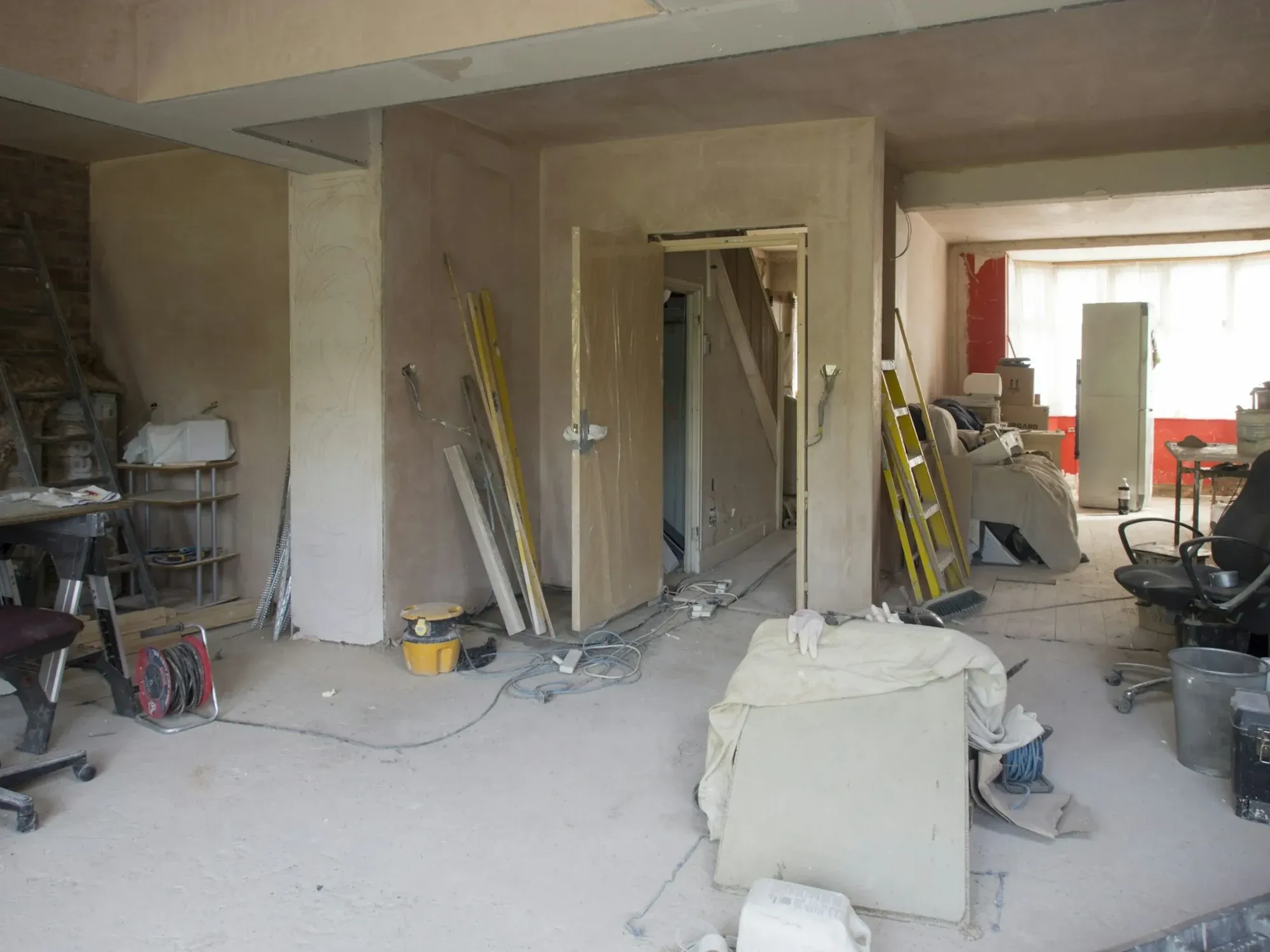 Interior under refurbishment, with bare plaster walls, ladders, tools and dust sheets
