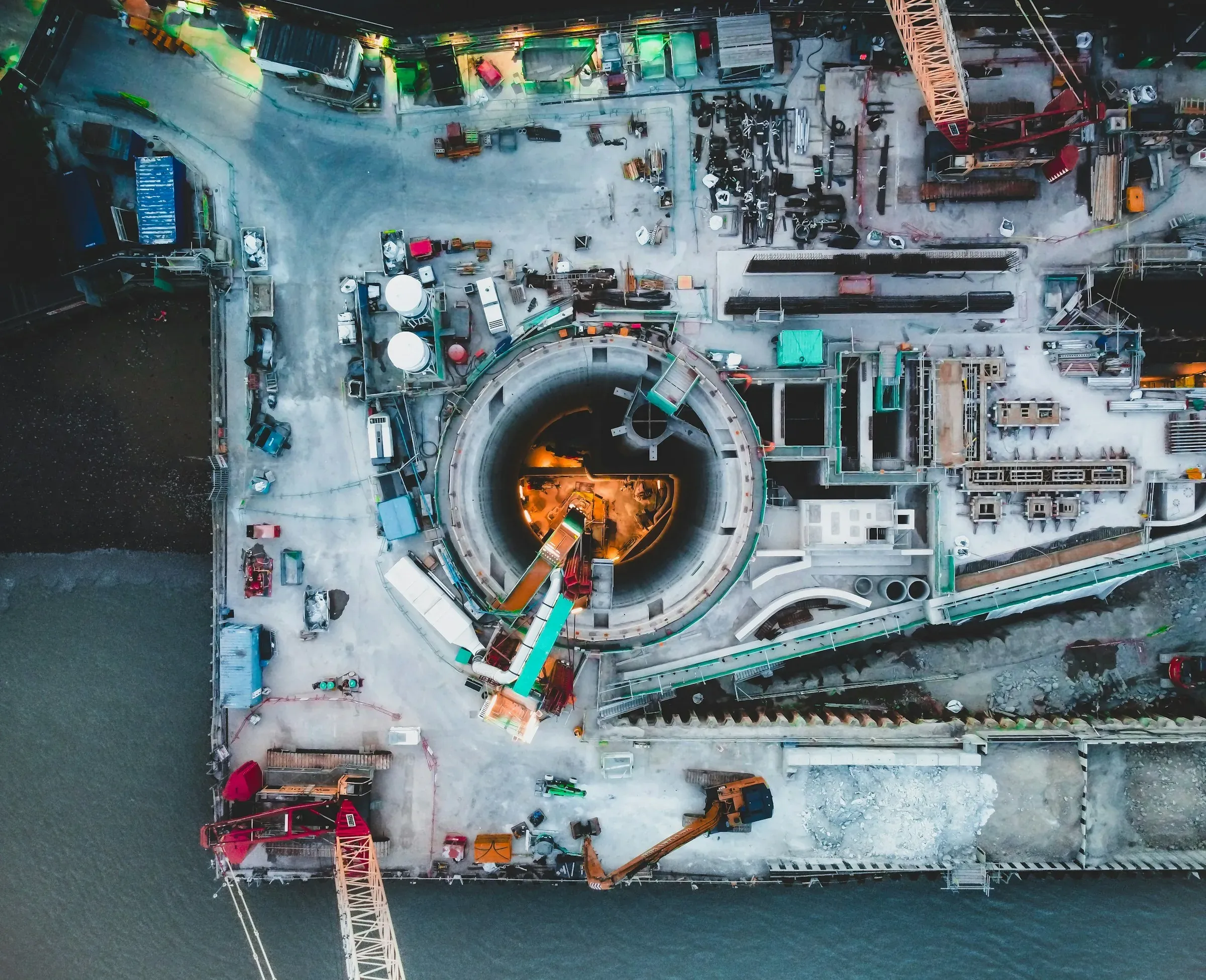 Aerial view of a riverside London site with a deep circular shaft and plant around it