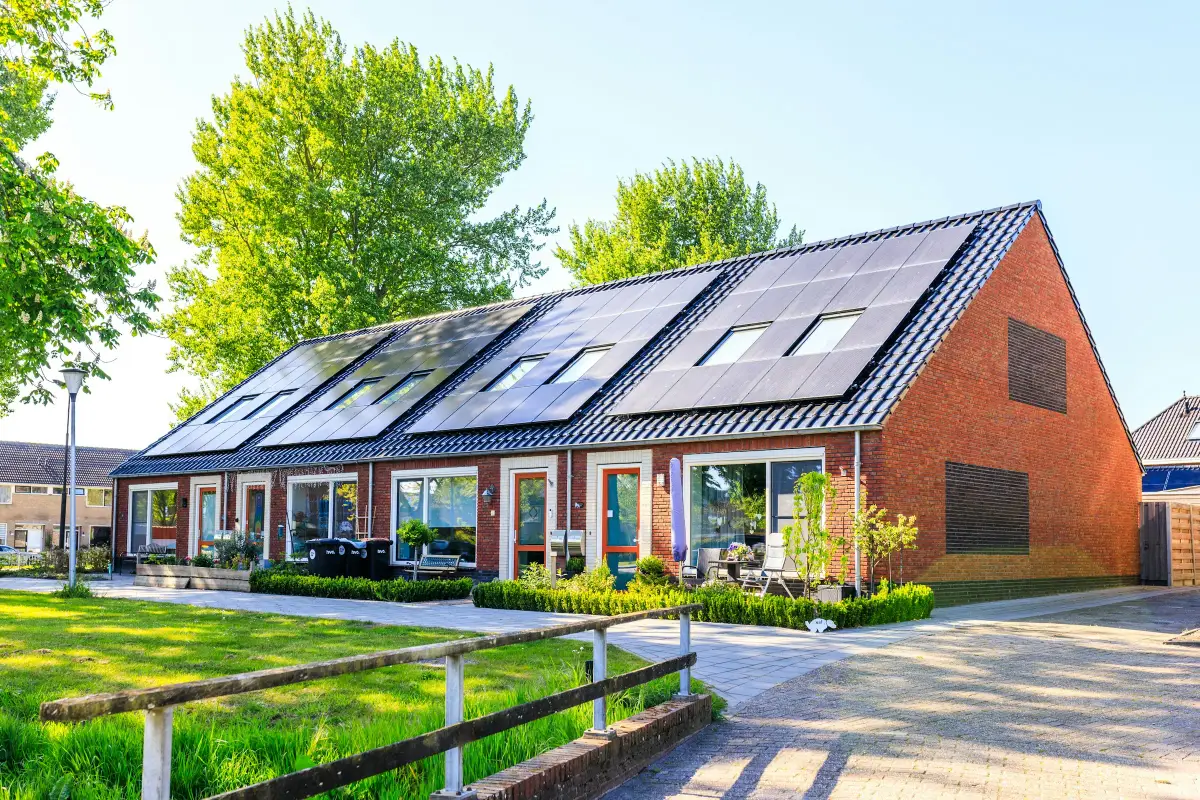 Row of red brick terraced houses with black solar panels and roof windows on a tiled roof