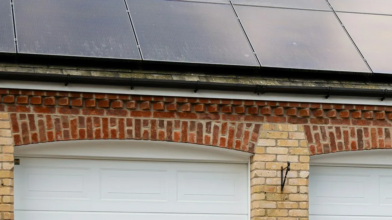 Black solar panels on a slate roof above a brick garage with white arched doors