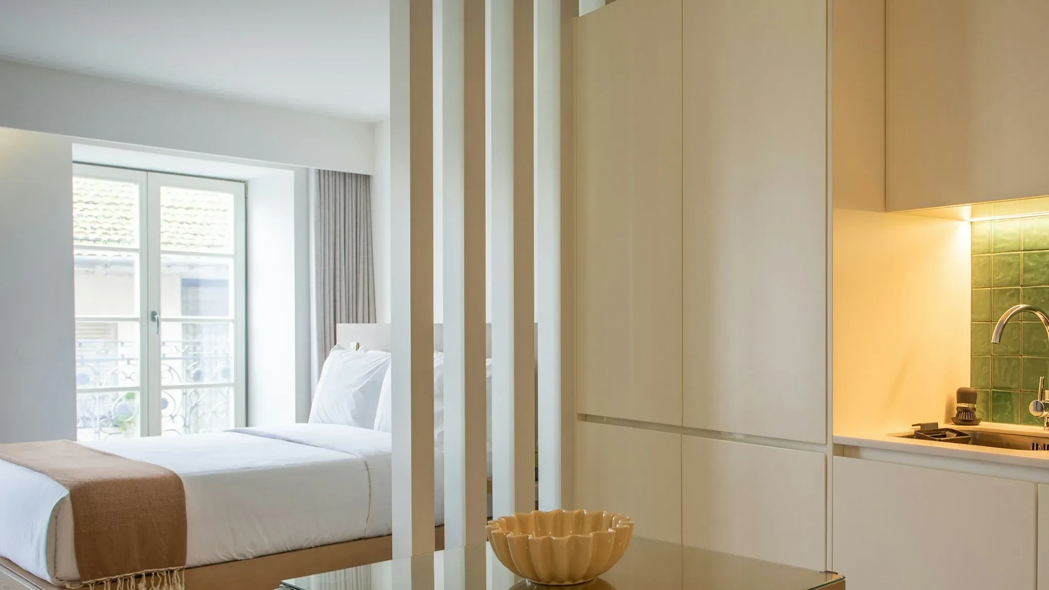 A compact studio with a slatted partition, a dining table and a white kitchen: the kind of room a refurbishment upgrades