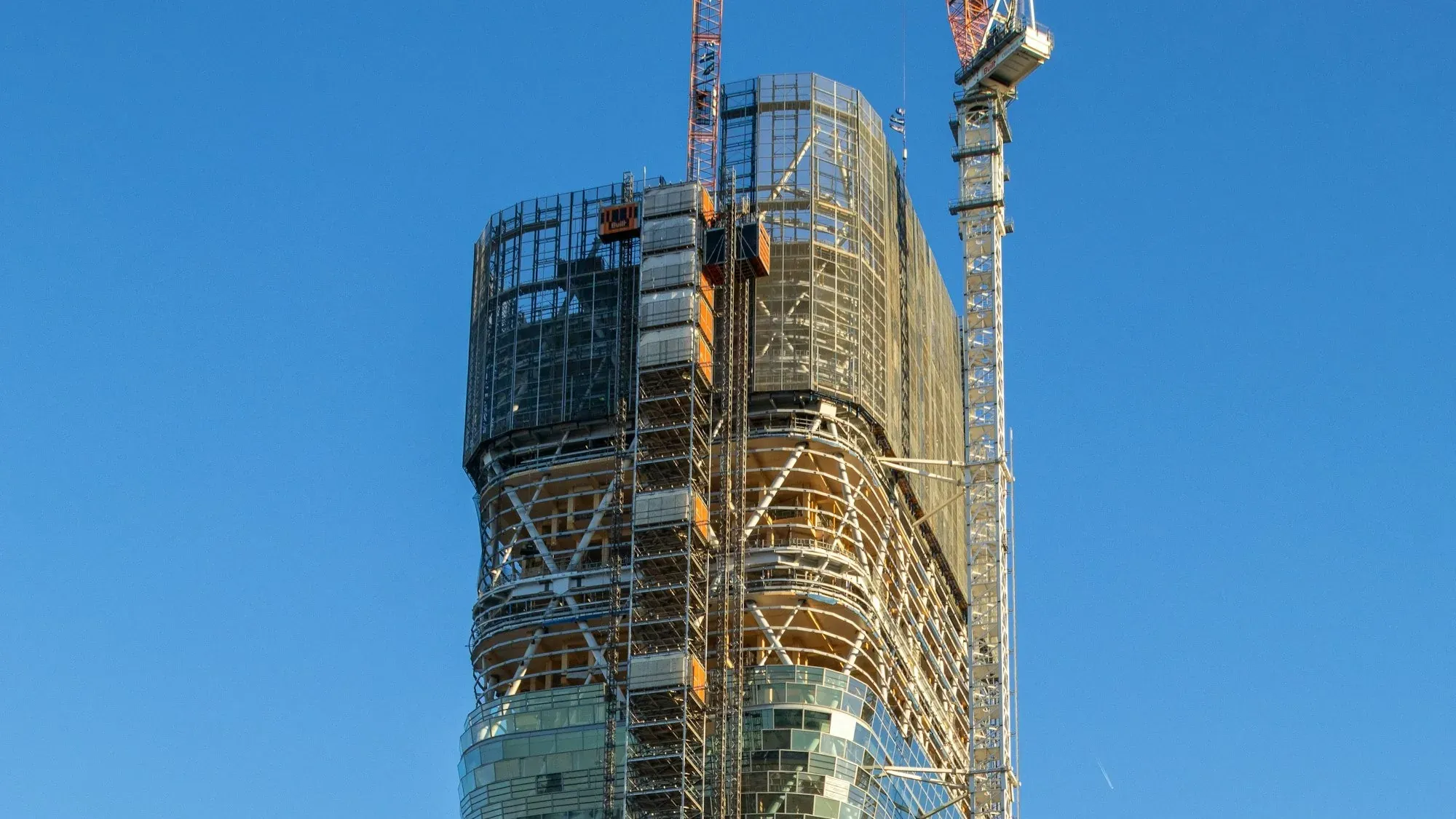 High-rise tower under construction with a tower crane and scaffolding against a blue sky