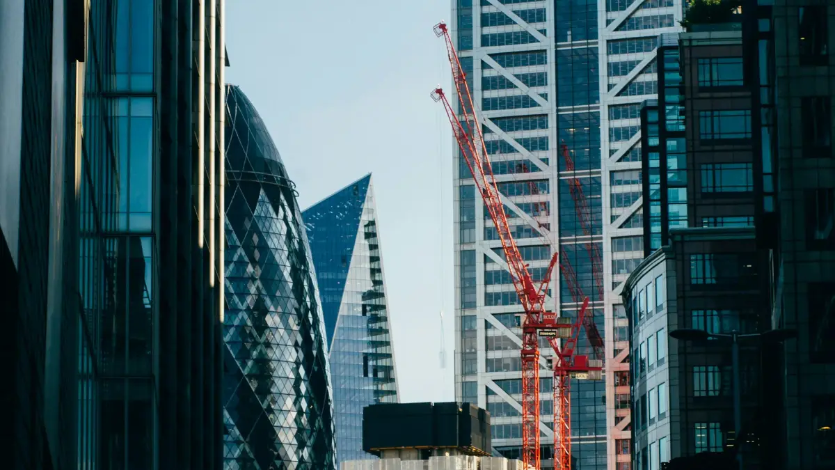 Red tower cranes beside City of London office towers seen from a street near Liverpool Street