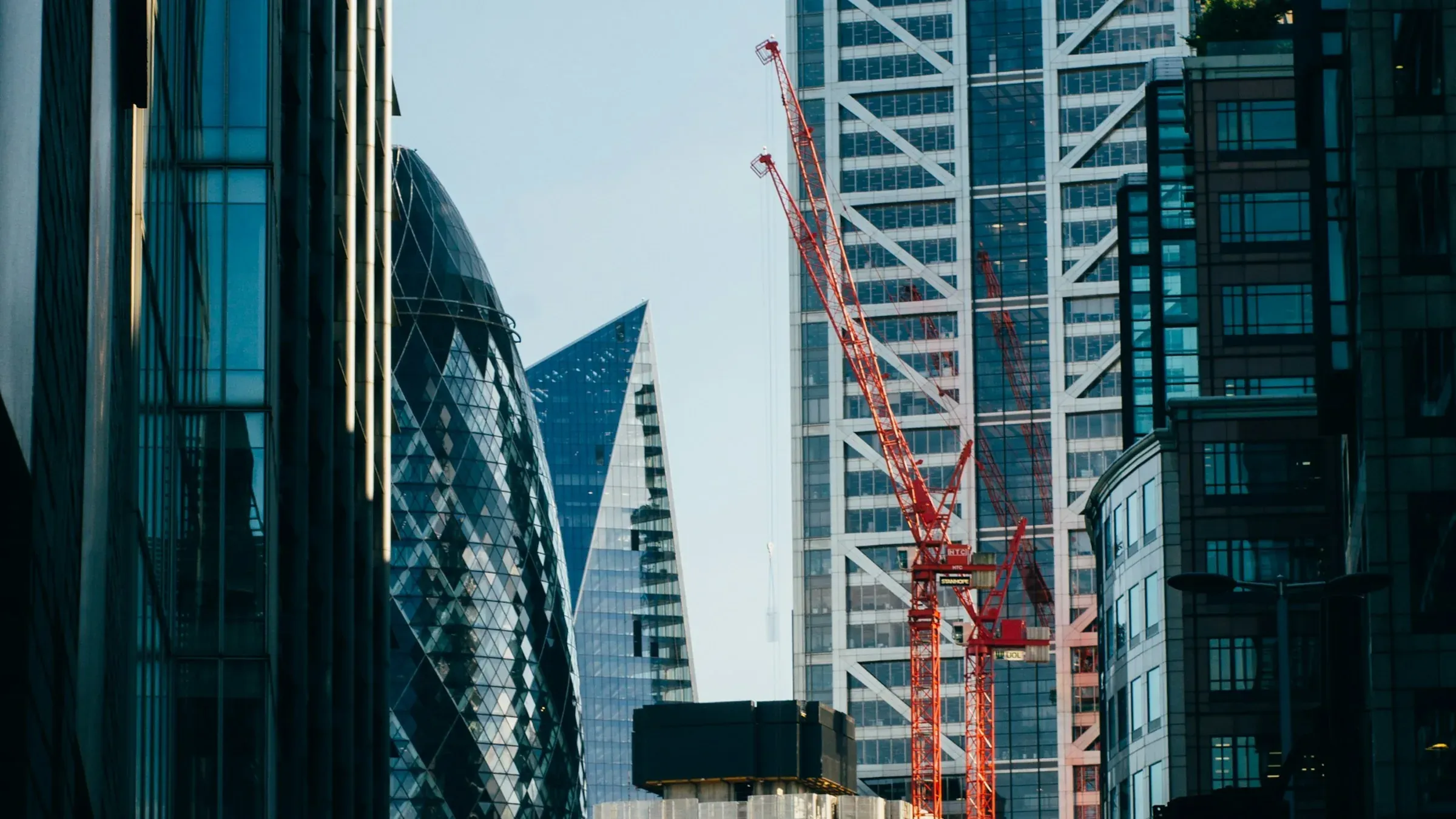 Red tower cranes beside City of London office towers seen from a street near Liverpool Street