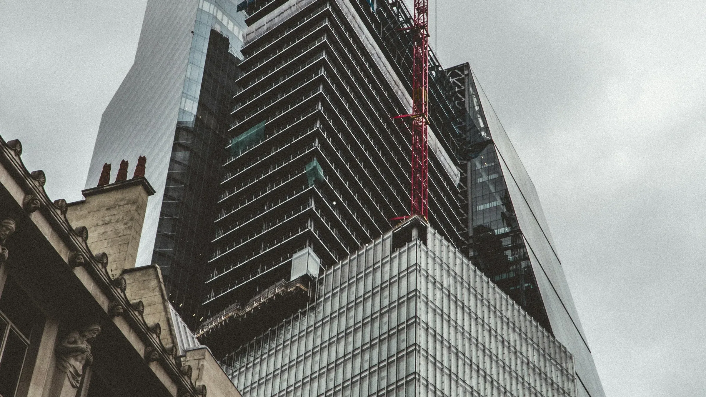 Concrete and steel frame of a City of London tower rising behind period buildings, glazing being fitted to the lower floors