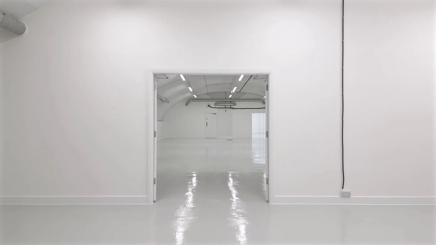 A fitted-out warehouse in a London railway arch: white walls, linear lighting and a resin floor seen through open double doors